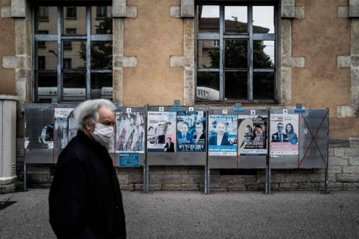 A man wearing a mask walks past electoral placards in Lyon on May 11, 2020, on the first day of France's easing of lockdown measures in place for 55 days to curb the spread of the COVID-19 pandemic, caused by the novel coronavirus. (Photo by JEFF PACHOUD / AFP)