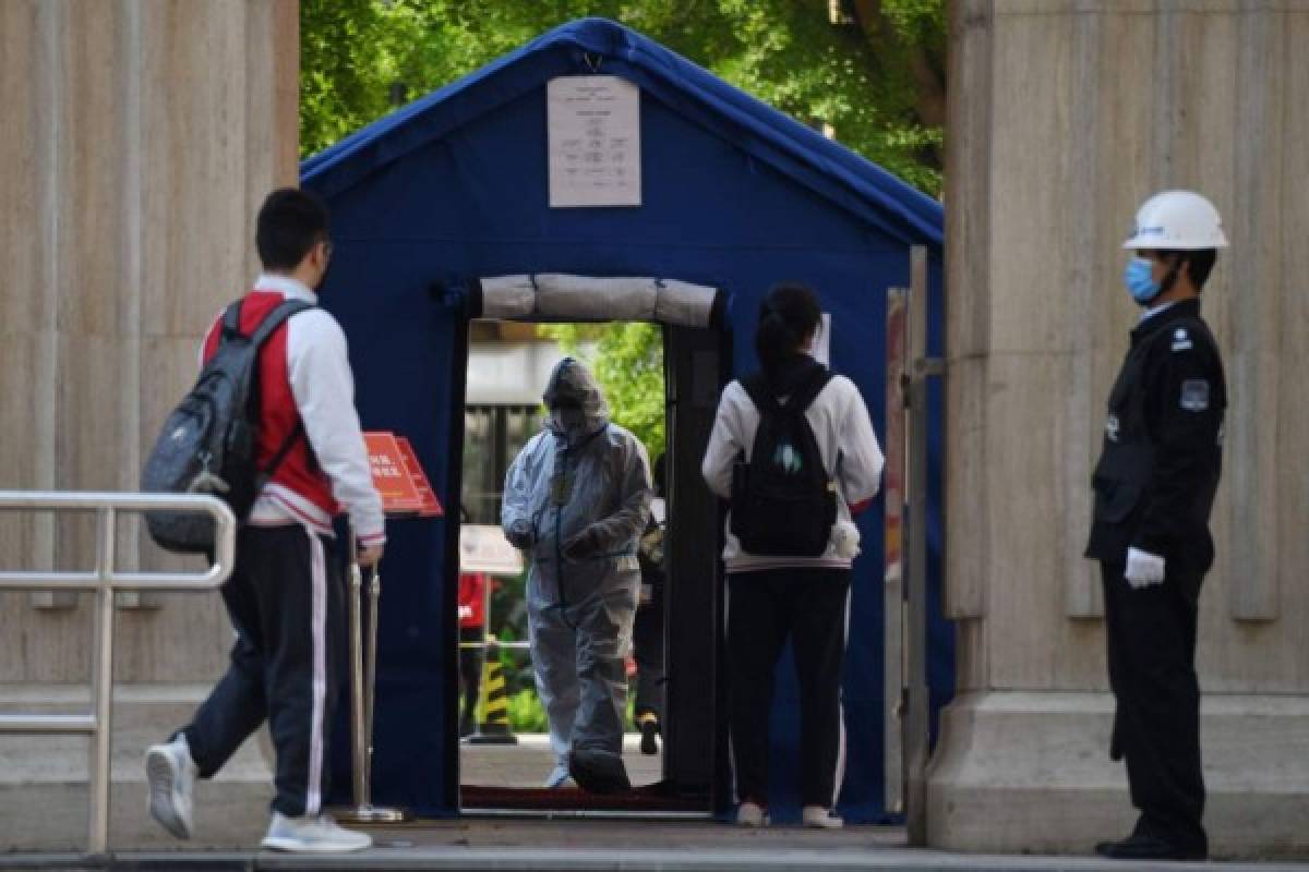 An official (C) in a hazmat suit waits inside a high school entrance as students arrive in Beijing on April 27, 2020. - Senior students returned to class on April 27 for the first time since schools were closed down in January as part of efforts to stop the spread of the COVID-19 coronavirus. (Photo by GREG BAKER / AFP)