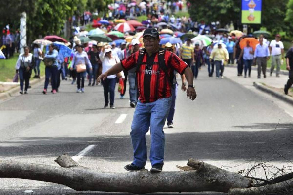 A man jumps over a tree trunk during a demonstration of members of education and health sectors against government reforms in Tegucigalpa, on June 18, 2019. - Thousands of teachers, doctors and students have been staging protests against the government of Honduran President Juan Orlando Hernandez for measures they say will privatize health and education services. (Photo by ORLANDO SIERRA / AFP)