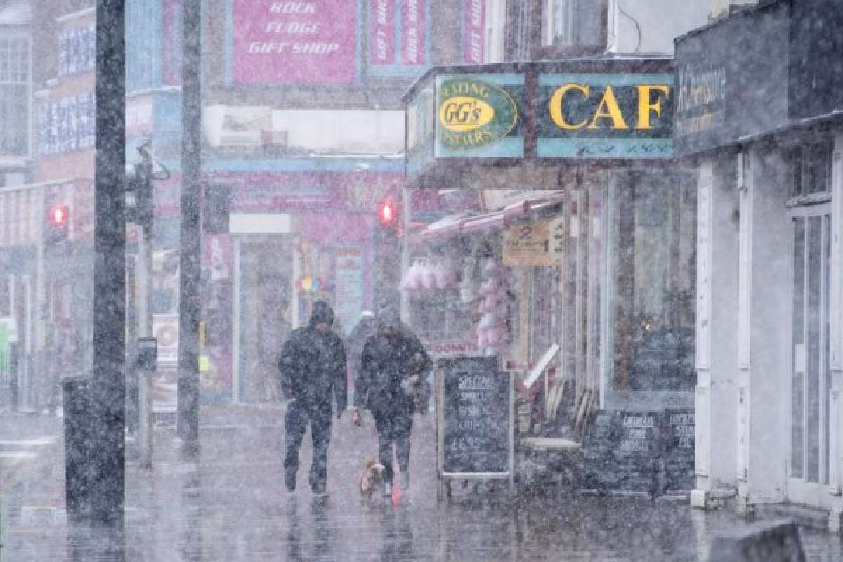 People walk along the promenade as heavy snow falls in the sea side resort of Scarborough in North Yorkshire on February 27, 2018. A blast of Siberian weather sent temperatures plunging across much of Europe on Tuesday, causing headaches for travellers and leading to several deaths from exposure as snow carpeted palm-lined Mediterranean beaches. / AFP PHOTO / Anthony Devlin