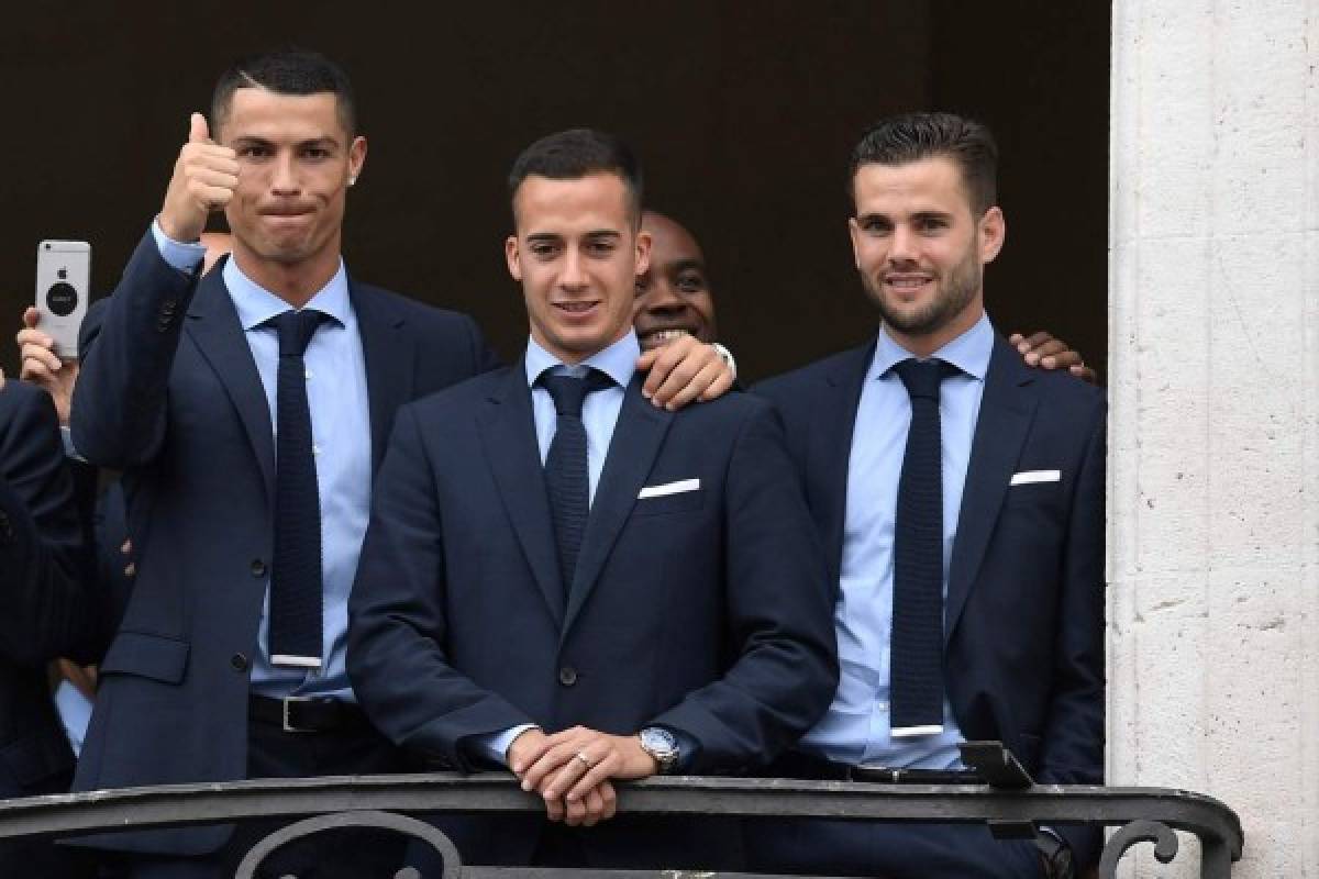 Real Madrid's Portuguese forward Cristiano Ronaldo (L) gives the thumbs up next to Real Madrid's Spanish midfielder Lucas Vazquez and Real Madrid's Spanish defender Nacho Fernandez from the balcony of the headquarters of the regional government of Madrid at the Puerta del Sol square in Madrid on May 27, 2018 as they celebrate their third Champions League title in a row in Kiev. / AFP PHOTO / OSCAR DEL POZO