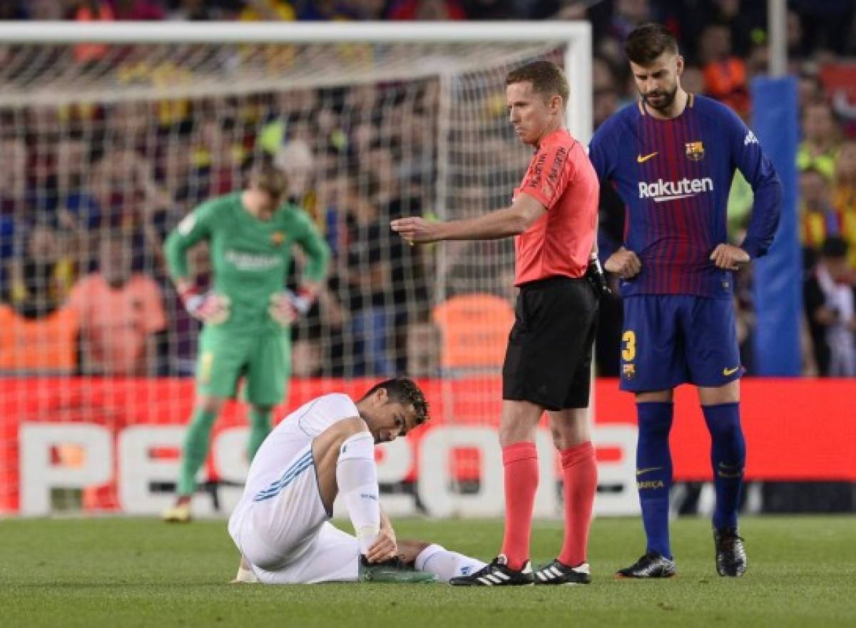 Real Madrid's Portuguese forward Cristiano Ronaldo (L) sits on the field after resulting injured dbeside Spanish referee Hernandez Hernandez (C) and Barcelona's Spanish defender Gerard Pique uring the Spanish league football match between FC Barcelona and Real Madrid CF at the Camp Nou stadium in Barcelona on May 6, 2018. / AFP PHOTO / Josep LAGO