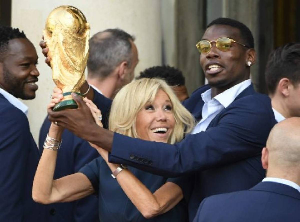 French President Emmanuel Macron's wife Brigitte Macron (C) holds the trophy next to France's midfielder Paul Pogba (R) during a reception at the Elysee Presidential Palace on July 16, 2018 in Paris, after French players won the Russia 2018 World Cup final football match. France celebrated their second World Cup win 20 years after their maiden triumph on July 15, 2018, overcoming a passionate Croatia side 4-2 in one of the most gripping finals in recent history. / AFP PHOTO / Lionel BONAVENTURE