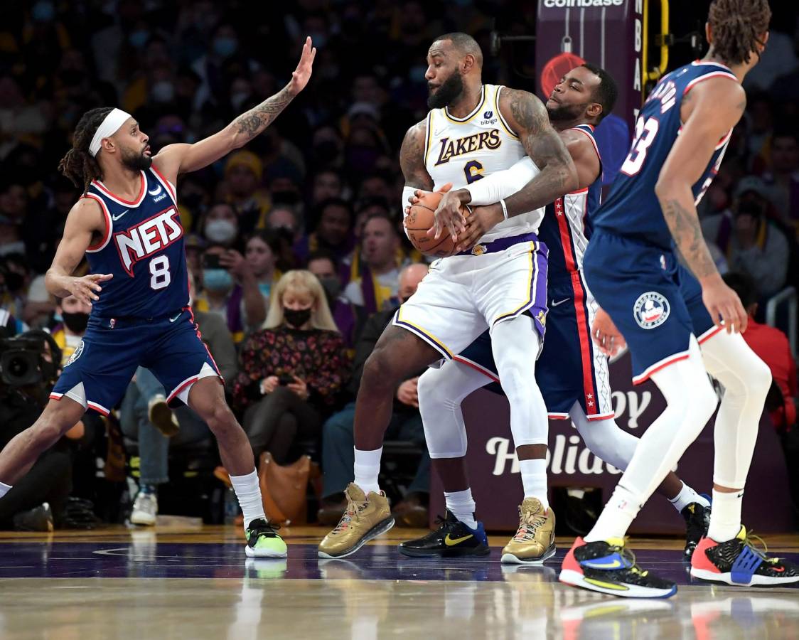 Patty Mills # 8 y Paul Millsap # 31 de los Brooklyn Nets defienden a LeBron James # 6 de Los Angeles Lakers mientras conduce hacia la canasta en la primera mitad del juego.