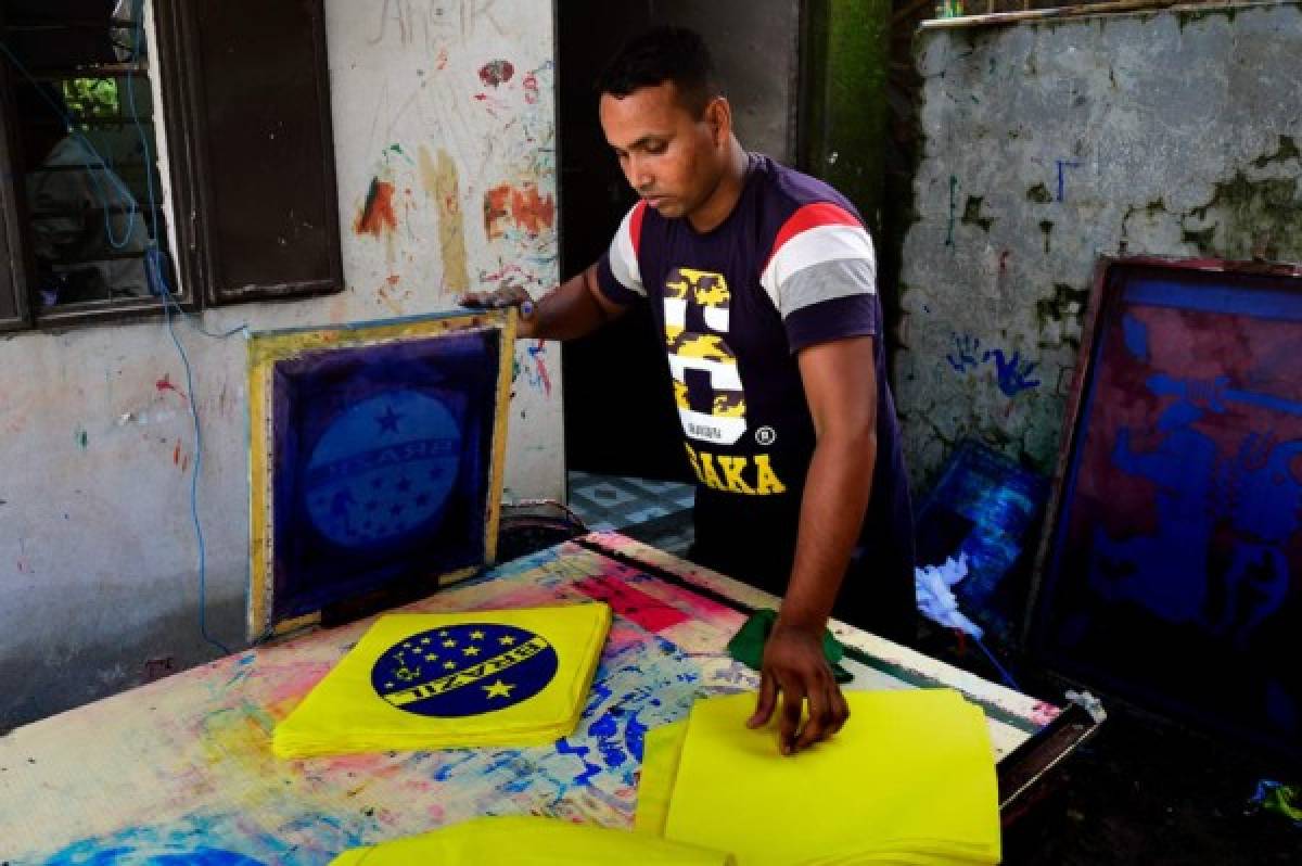 This photograph taken on May 17, 2018, shows a Bangladeshi worker using a silk-screen for printing a Brazil flag in Narayanganj, on the outskirts of Dhaka, ahead of the 2018 football World Cup. Flag makers in Bangladesh are doing a roaring trade weeks ahead of the World Cup, but no-one is interested in the home nation's colours -- the money is all on pennants for Lionel Messi's Argentina and Neymar's Brazil. / AFP PHOTO / Munir UZ ZAMAN / TO GO WITH AFP STORY FBL-WC-2018-BAN-BANGLADESH-FLAGS,FOCUS BY SHAFIQUL ALAM