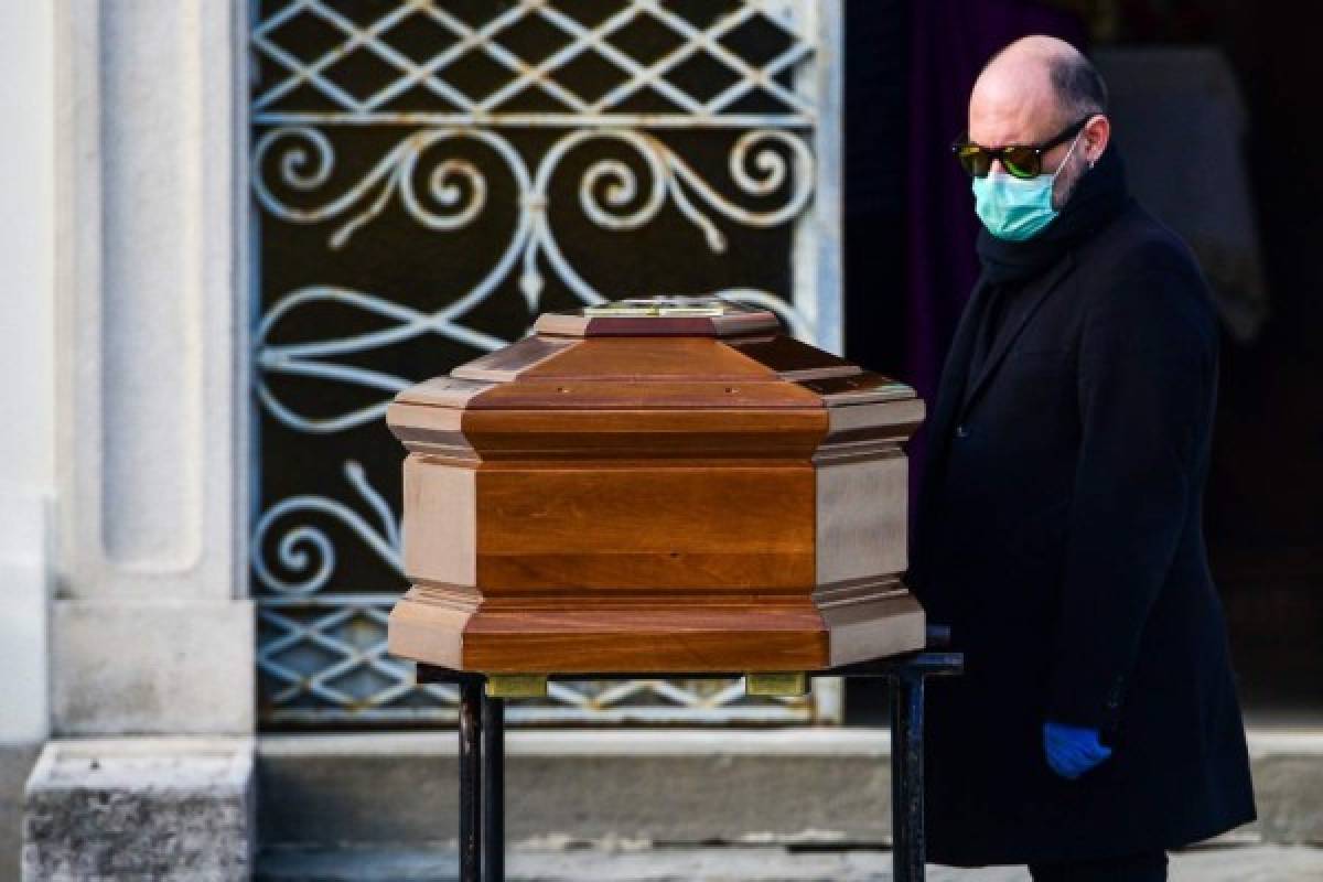 A man wearing a face mask stands by the coffin of his mother during a funeral service in the closed cemetery of Seriate, near Bergamo, Lombardy, on March 20, 2020 during the country's lockdown aimed at stopping the spread of the COVID-19 (new coronavirus) pandemic. (Photo by Piero Cruciatti / AFP)