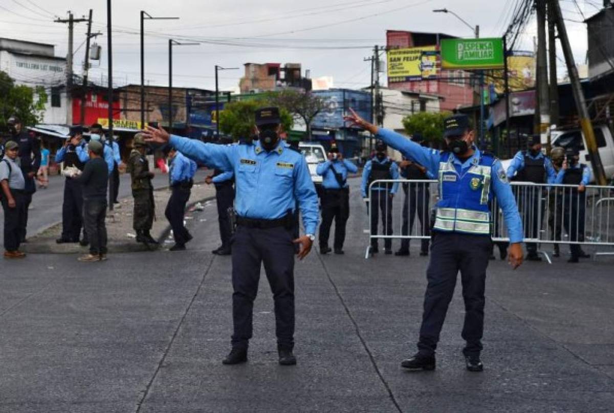 National Police officers wearing face masks as a preventive measure against the spread of the new coronavirus, COVID-19, divert traffic at a blocked avenue during the curfew against the disease, in Tegucigalpa on March 24, 2020. - Days ago, the government decreed 'an absolute curfew' to force the population to isolate themselves in their homes and curb the spread of the virus in the poor Central American country (Photo by Orlando SIERRA / AFP)