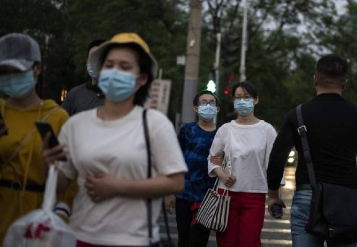 People wearing face masks walk along a street in Beijing on May 1, 2020. (Photo by NOEL CELIS / AFP)