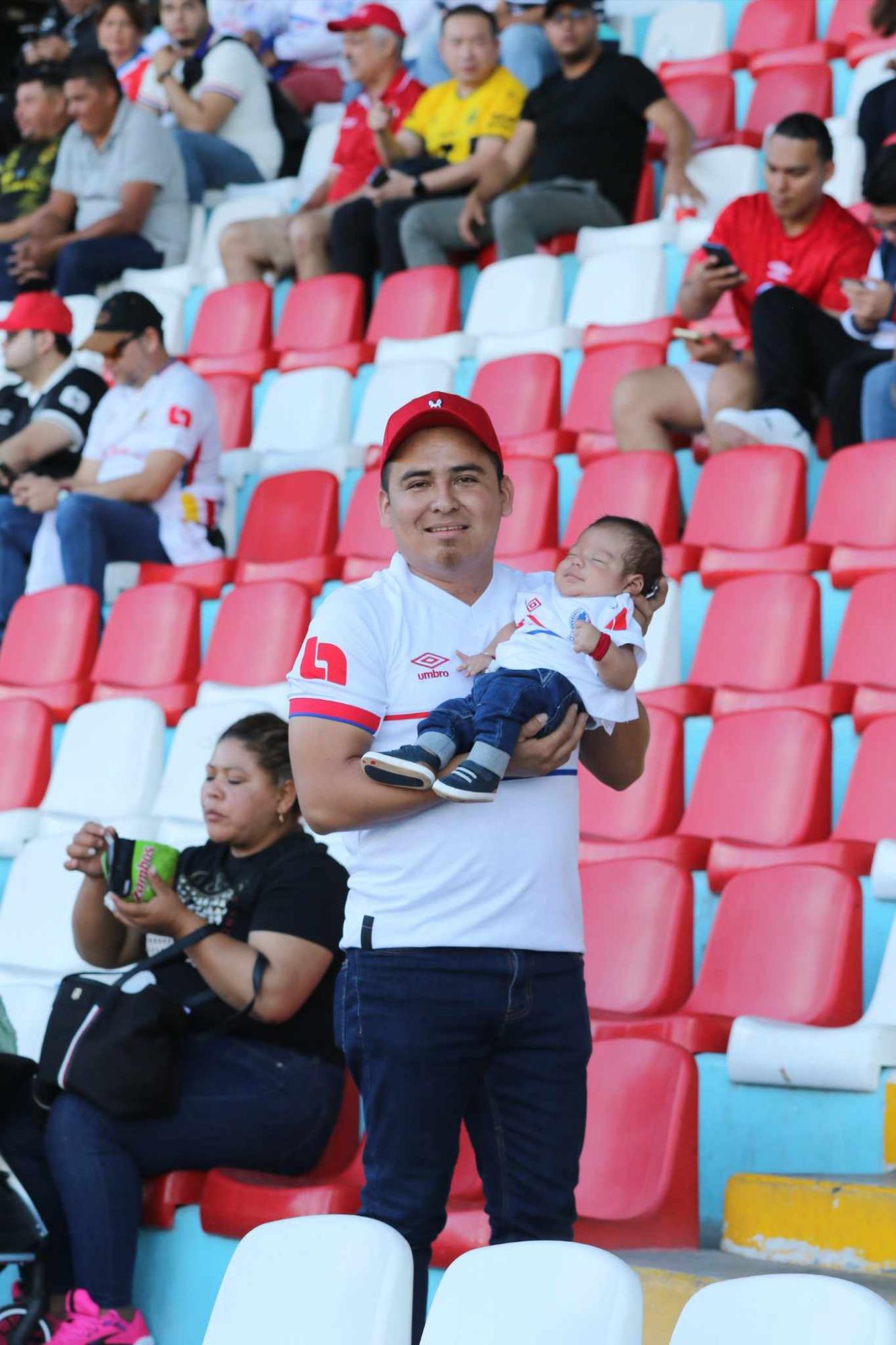 Un padre muy orgulloso con su bebé, ambos bien identificados con la camisa del Olimpia.