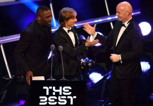 British actor and event host Idris Elba (L) speaks as Real Madrid and Croatia midfielder Luka Modric (C) and FIFA president Gianni Infantino (R) shake hands after Modric wins the trophy for the Best FIFA Men's Player of 2018 Award during The Best FIFA Football Awards ceremony, on September 24, 2018 in London. / AFP PHOTO / Ben STANSALL