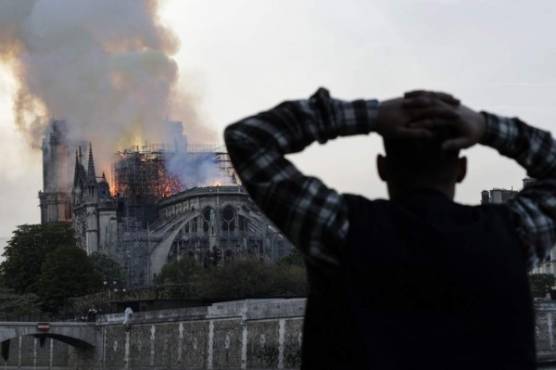 A man watches the landmark Notre-Dame Cathedral burn, engulfed in flames, in central Paris on April 15, 2019. - A huge fire swept through the roof of the famed Notre-Dame Cathedral in central Paris on April 15, 2019, sending flames and huge clouds of grey smoke billowing into the sky. The flames and smoke plumed from the spire and roof of the gothic cathedral, visited by millions of people a year. A spokesman for the cathedral told AFP that the wooden structure supporting the roof was being gutted by the blaze. (Photo by Geoffroy VAN DER HASSELT / AFP)