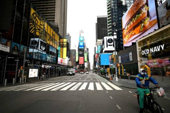 A man bikes through the deserted Times Square on April 10, 2020 in New York City. - The global coronavirus death toll topped 100,000 on April 10 as Easter celebrations around the world kicked off in near-empty churches with billions of people stuck indoors to halt the pandemic's deadly worldwide march. (Photo by Johannes EISELE / AFP)