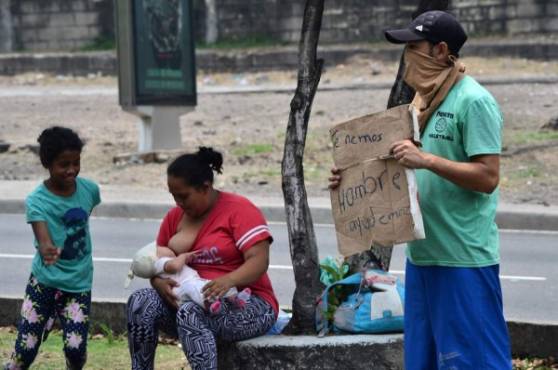 Honduran Cintia Suyapa Zelaya (L) breastfeeds her baby girl Valentina, next to her husband Obdulio Garcia and their daughter Elena Milagro while begging for money with a sign reading We are hungry. Help us along the 'Fuerzas Armadas' boulevard on the eve of Mother's Day, in Tegucigalpa, on May 9, 2020, amid the new coronavirus pandemic. - Suyapa Zelaya, 24, admits she violates the curfew imposed by the government in the fight against the new coronavirus because she has to beg for money to eat. (Photo by ORLANDO SIERRA / AFP)