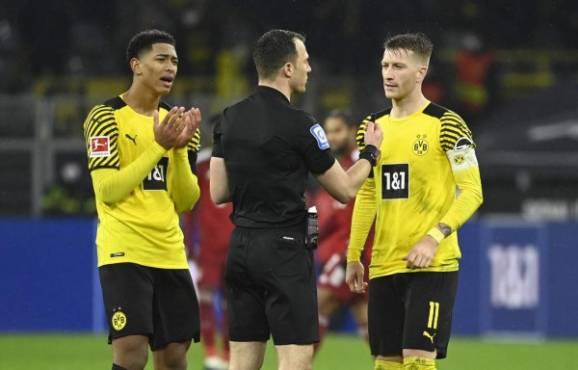 Dortmund's English midfielder Jude Bellingham (L) and Dortmund's German forward Marco Reus (R) discuss with referee Felix Zwayer after a deliberate handball during the German first division Bundesliga football match BVB Borussia Dortmund v FC Bayern Munich in Dortmund, western Germany, on December 3, 2021. (Photo by Ina FASSBENDER / AFP) / DFL REGULATIONS PROHIBIT ANY USE OF PHOTOGRAPHS AS IMAGE SEQUENCES AND/OR QUASI-VIDEO