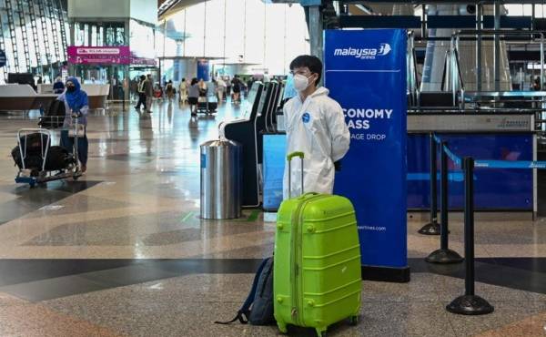 $!A passenger wearing personal protective equipment (PPE) stands by his luggage at the Kuala Lumpur International Airport (KLIA) in Sepang on November 29, 2021, as countries across the globe shut borders and renewed travel curbs in response to the spread of a new, heavily mutated Covid-19 coronavirus variation dubbed Omicron. (Photo by Mohd RASFAN / AFP)